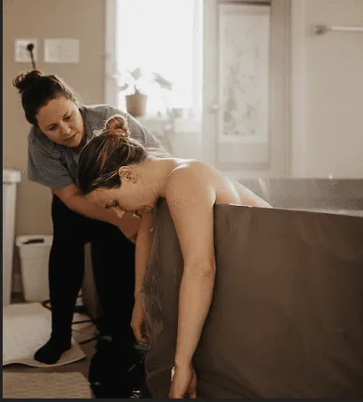 Accompagnante soutenant une femme en travail appuyée contre une baignoire