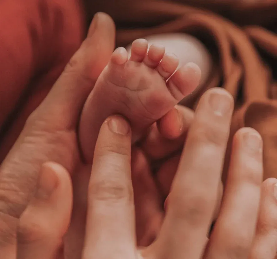 Pied de bébé tenu délicatement entre les mains d'une réflexologue