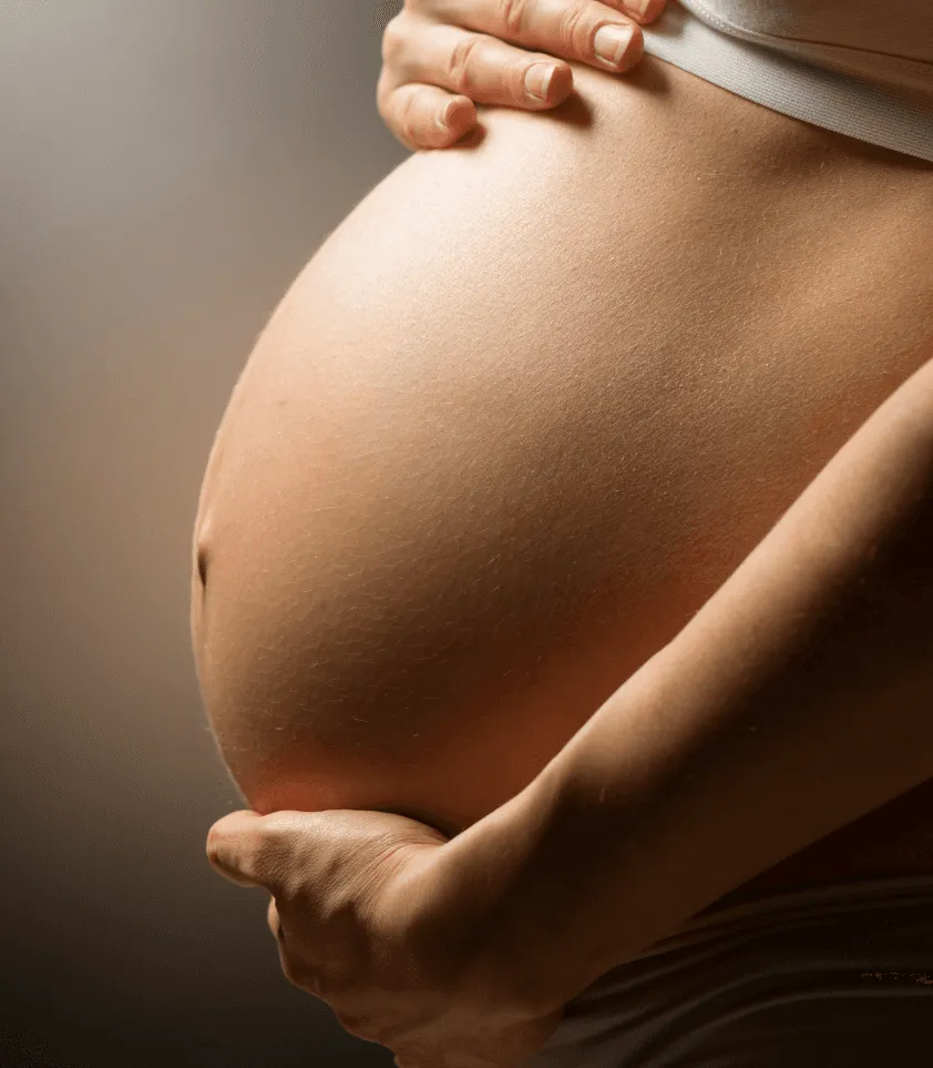 Ventre d'une femme enceinte en fin de grossesse, dans une lumière chaude