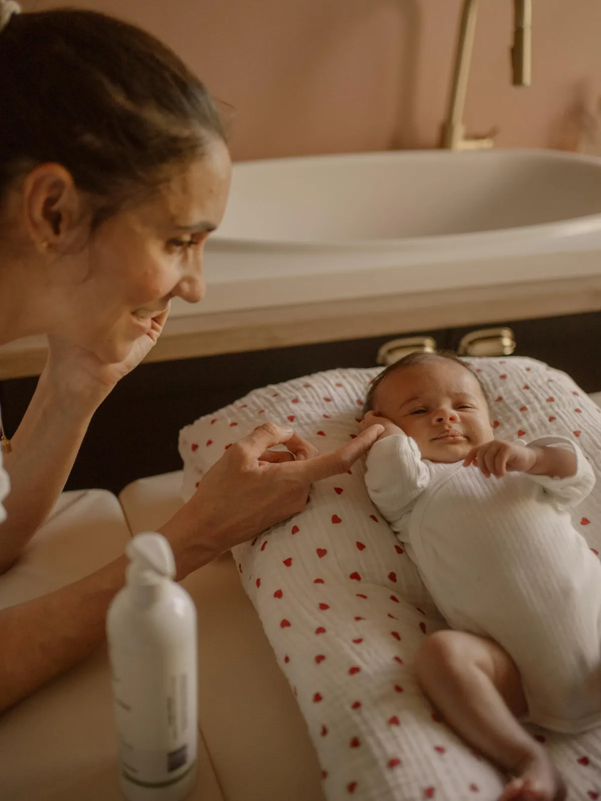 Formatrice souriant à un nouveau-né allongé sur un coussin, un flacon d'huile de massage au premier plan