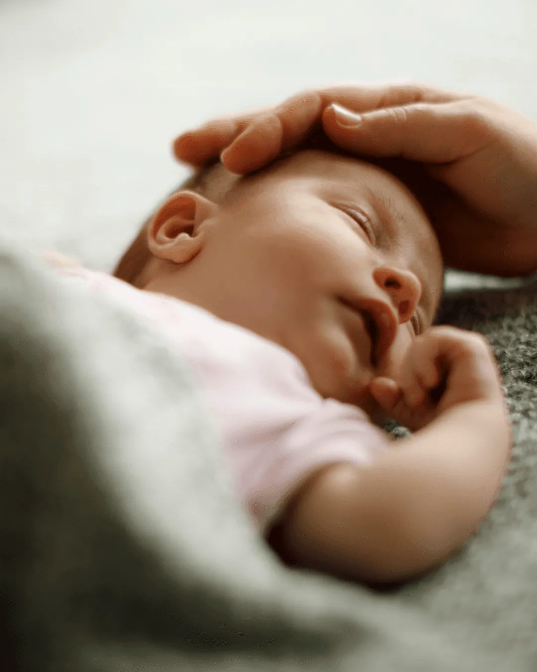Bébé endormi sur une couverture, une main caressant doucement sa tête