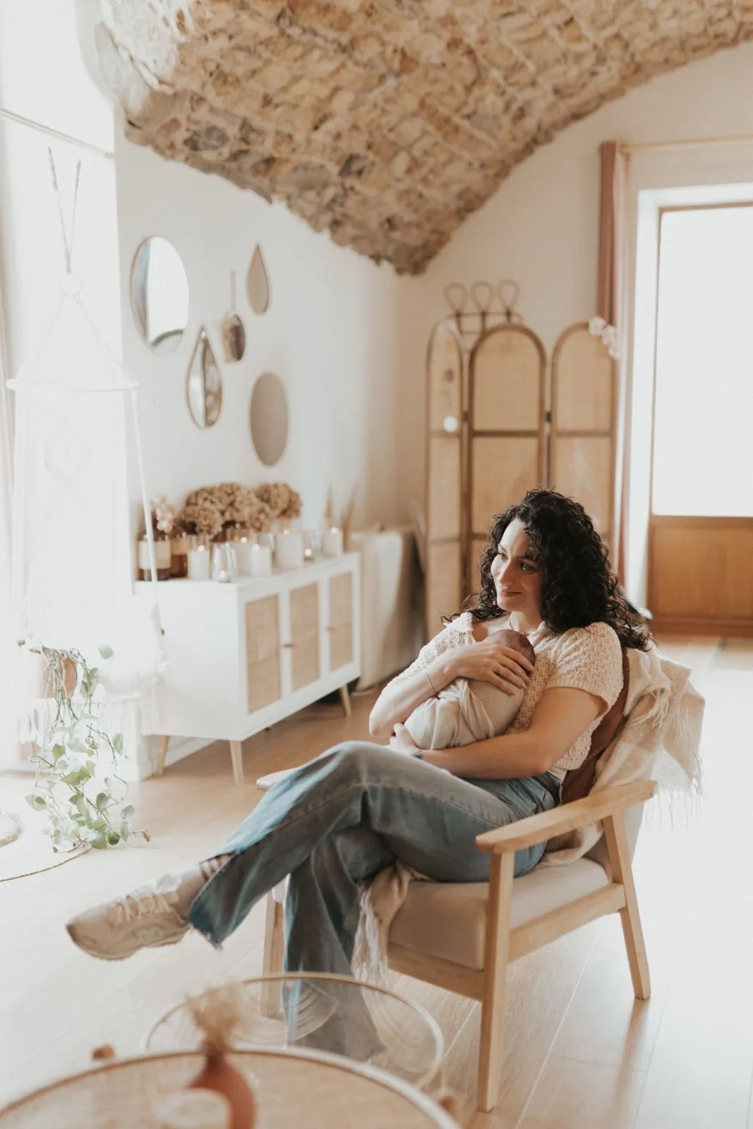 Mère assise dans un fauteuil avec son bébé contre elle, dans une pièce claire et apaisante