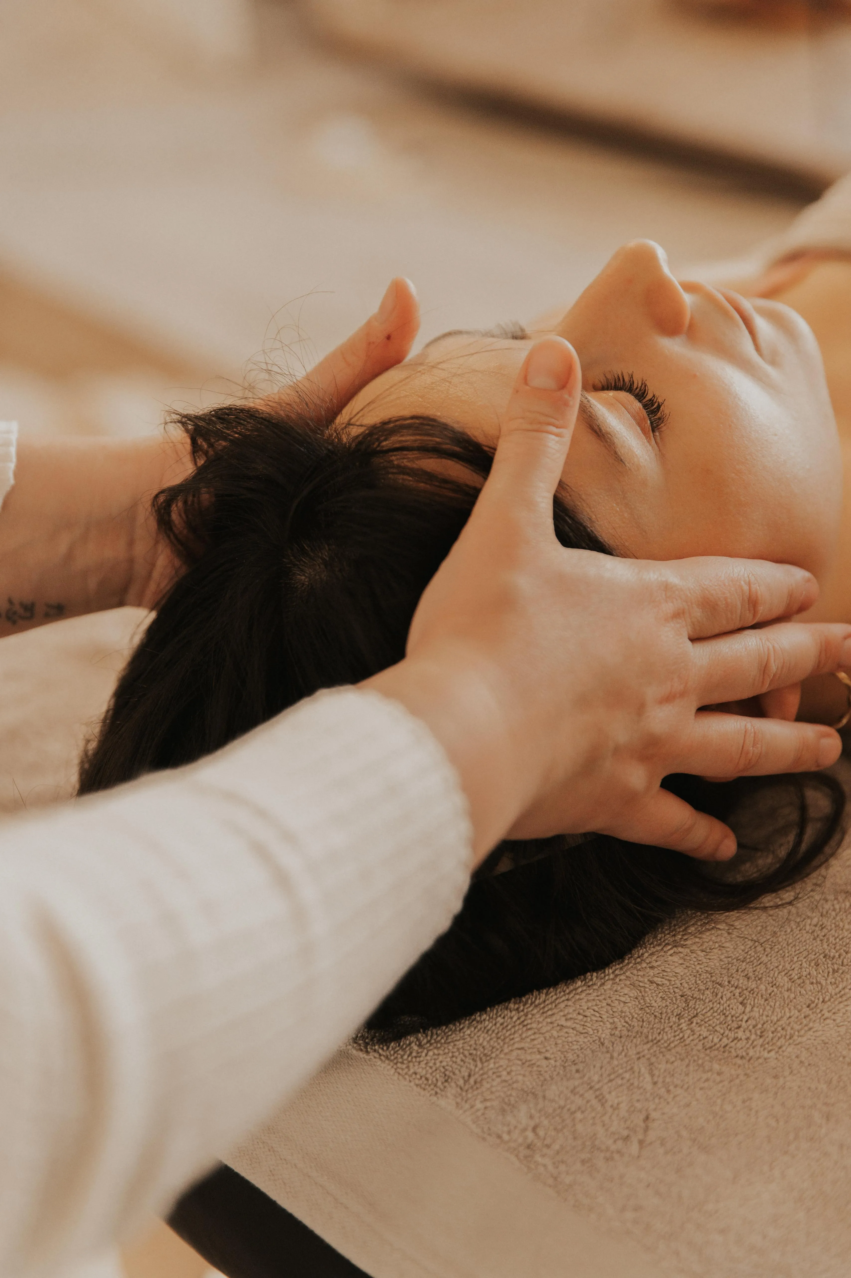 Soin du visage d'une jeune mère, mains de la praticienne posées sur ses tempes