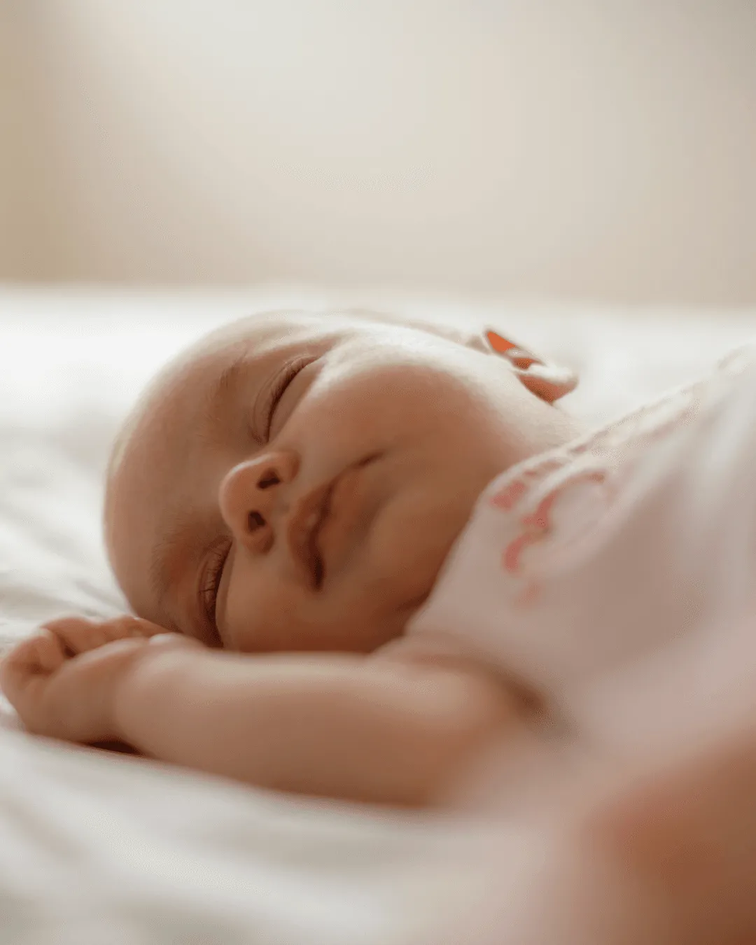 Bébé profondément endormi sur le dos dans un lit blanc, les bras près du visage