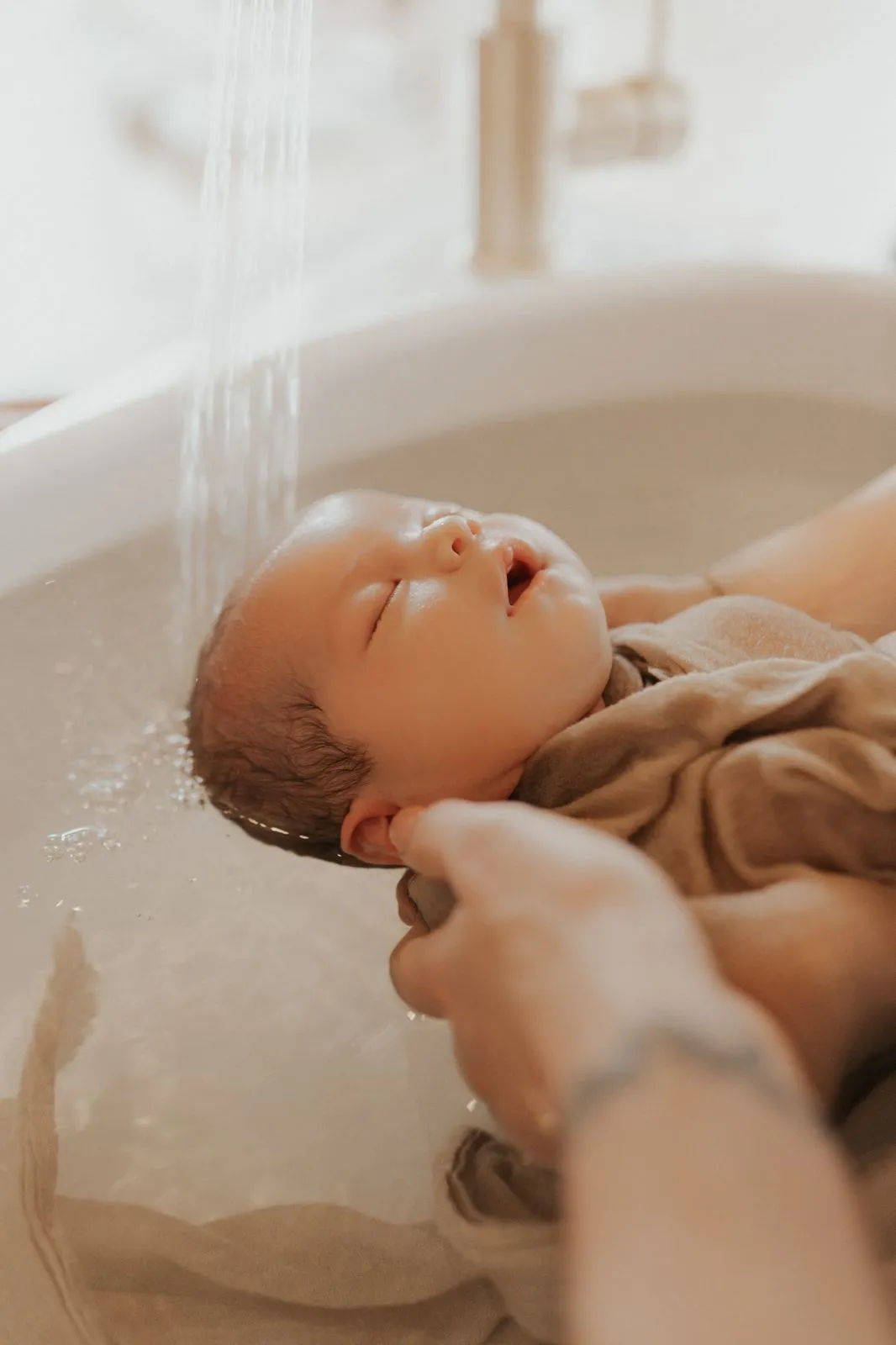 Nouveau-né dans son bain d'accueil, la tête soutenue par les mains de la praticienne