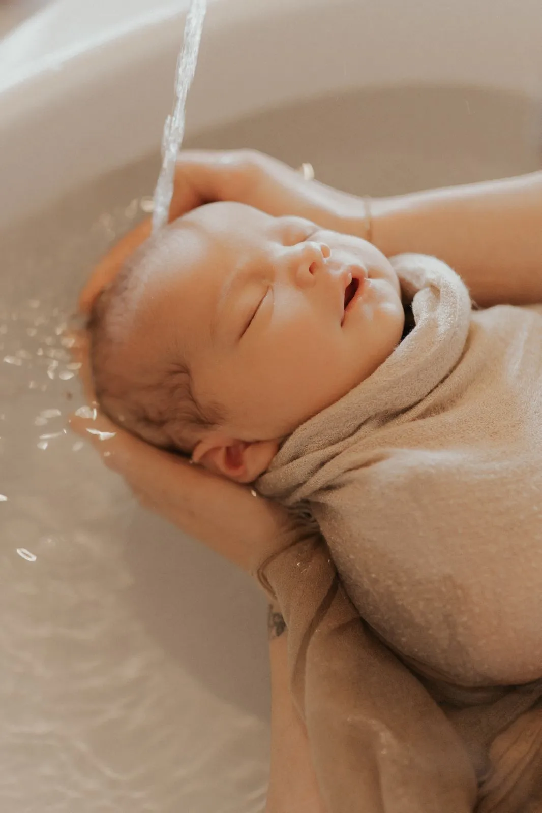 Bébé endormi soutenu dans l'eau par la praticienne pendant un bain d'accueil